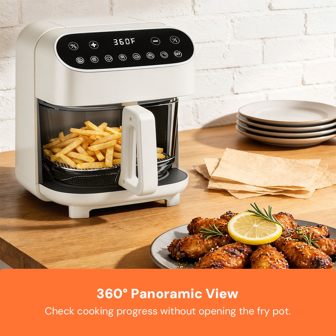 A white countertop air fryer with a black digital control panel sits on a wooden table, filled with french fries. A plate of glazed chicken with a lemon garnish and stacked plates are nearby, against a white brick wall background.