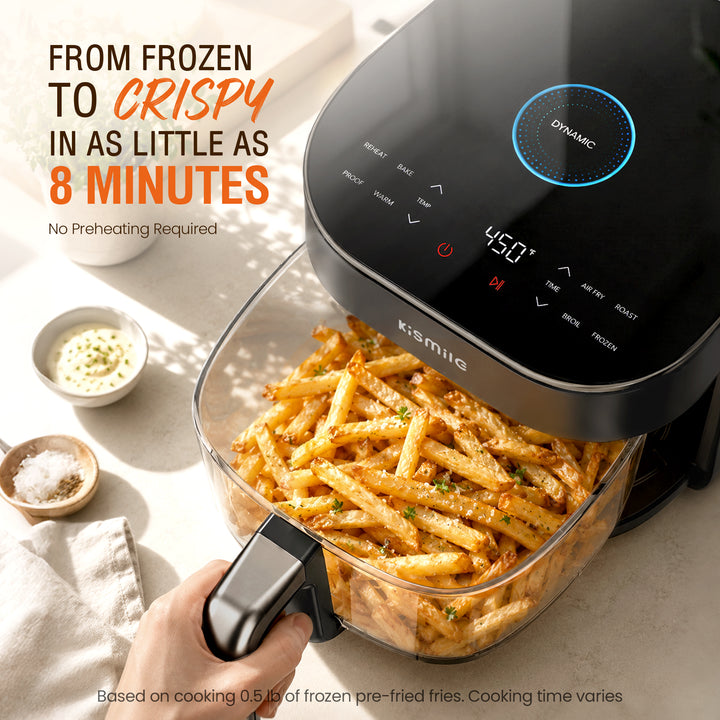 A Kismile air fryer with a clear basket filled with golden crispy fries, shown with a hand holding the handle. The background is a clean, sunlit kitchen counter with small bowls of seasoning and garlic sauce, alongside promotional text.