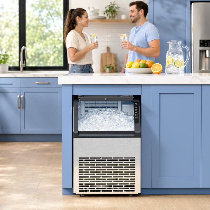 A countertop ice machine in a modern kitchen with blue cabinets, shown with a man and woman standing nearby holding glasses.