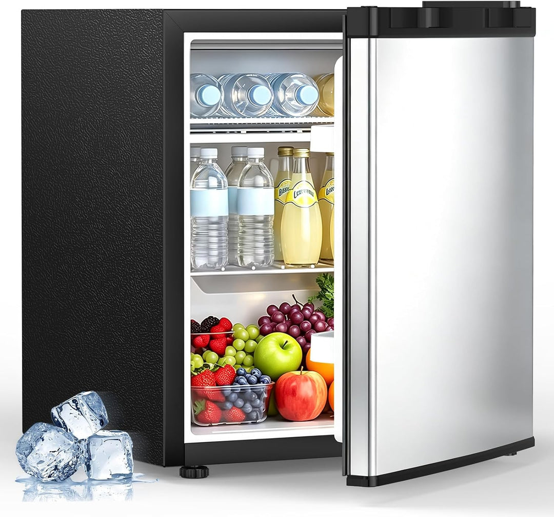 A compact mini refrigerator with a black textured exterior and a stainless steel door, shown open and stocked with bottled drinks, juice, fruit, and berries. Ice cubes are placed on the floor beside it, all on a clean white background.
