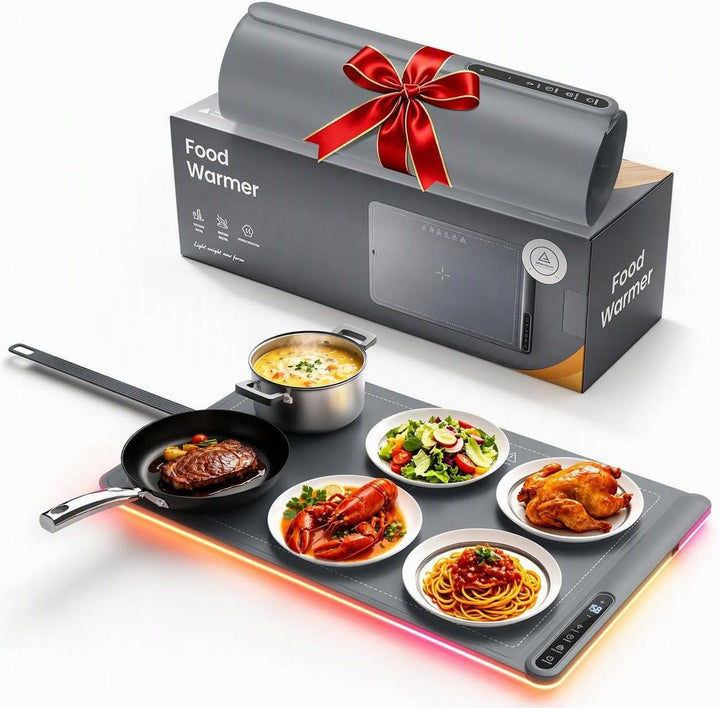 A countertop food warmer tray with five plates of food on a glowing pad, shown in front of its retail box wrapped with a red ribbon. The box is labeled 'Food Warmer' and 'KEMNA'.