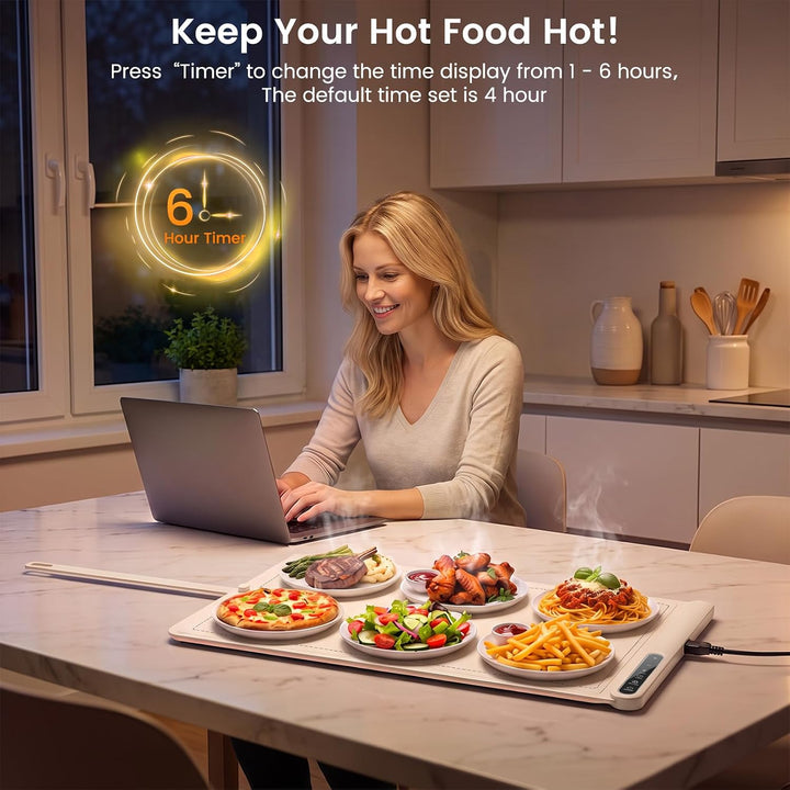 A woman sits at a kitchen table using a laptop while hot food sits on a heated tray on the table. Text at the top explains how to change the timer display, and the scene is set in a modern kitchen.