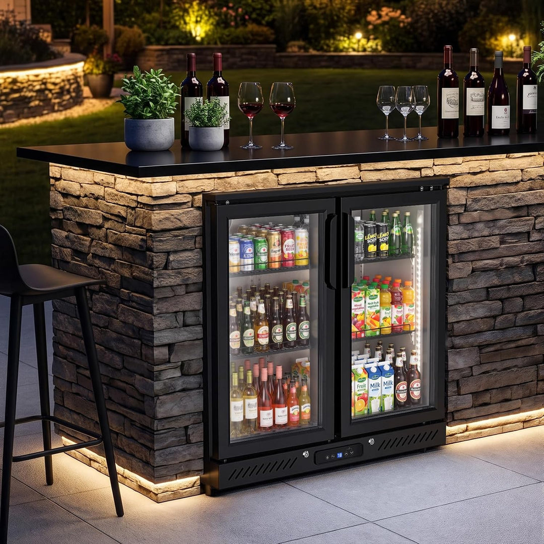 Underbar counter wine refrigerator with two glass doors, stocked with bottles, set into a stone bar island at night with lit wine glasses and bottles on top.