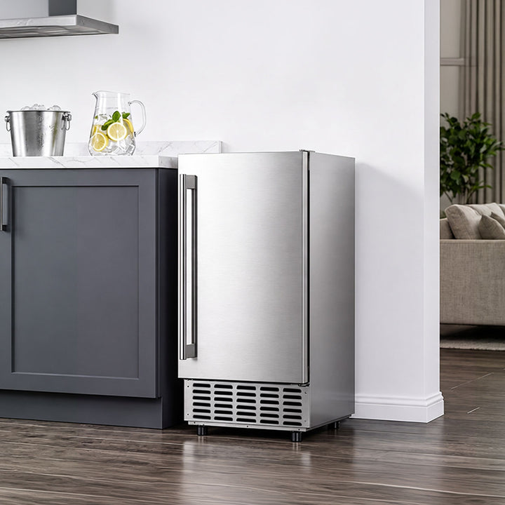 A stainless steel undercounter refrigerator with a single vertical handle, positioned next to a dark gray kitchen cabinet in a modern kitchen setting with wood floors.